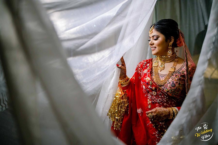 Bride Sanya in bridal attire framed by draped fabric during her wedding to Anish