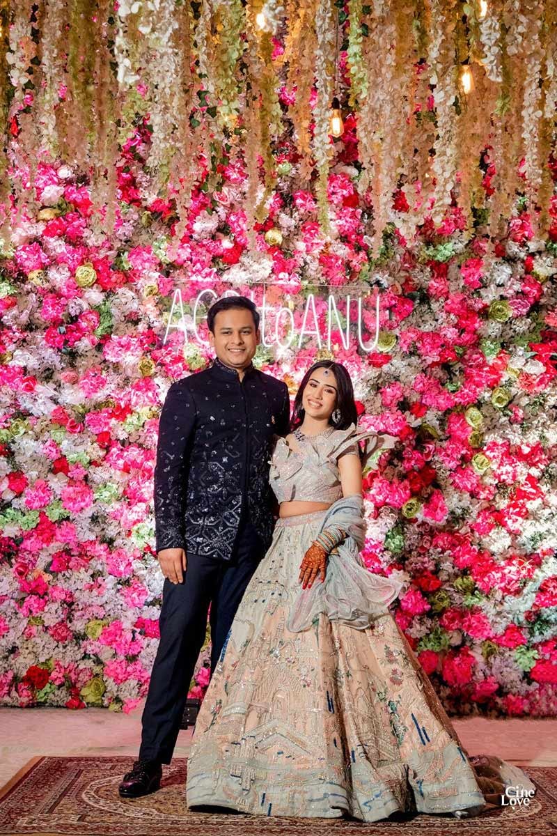 Bride and groom standing together against a floral wall backdrop
