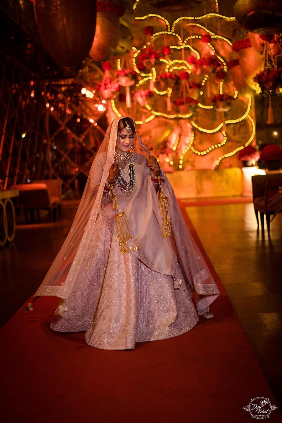 Bride Prakriti in an ornate embellished lehenga posing in a warmly lit setting at her wedding to Sahil