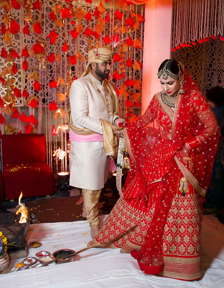 Ayushi and Shashwat in red traditional attire amid confetti at their wedding celebration