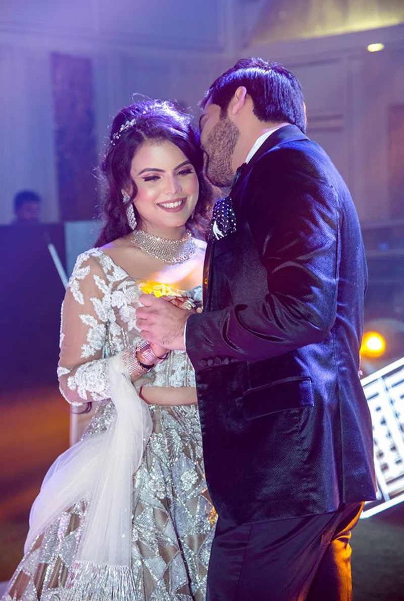 Bride Neha in a white gown under stage lighting at her reception