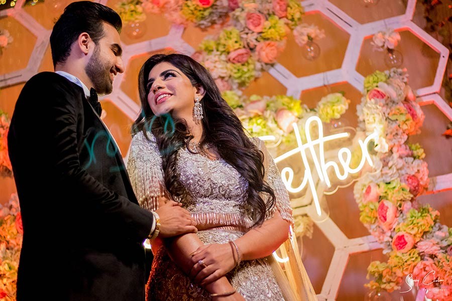 Bride in red lehenga and groom in black suit smiling together