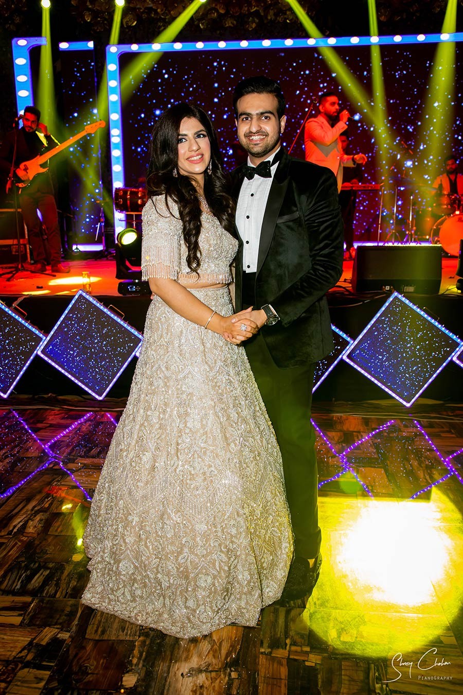 Vrinda and Mohit in cream attire against colorful decor at their wedding