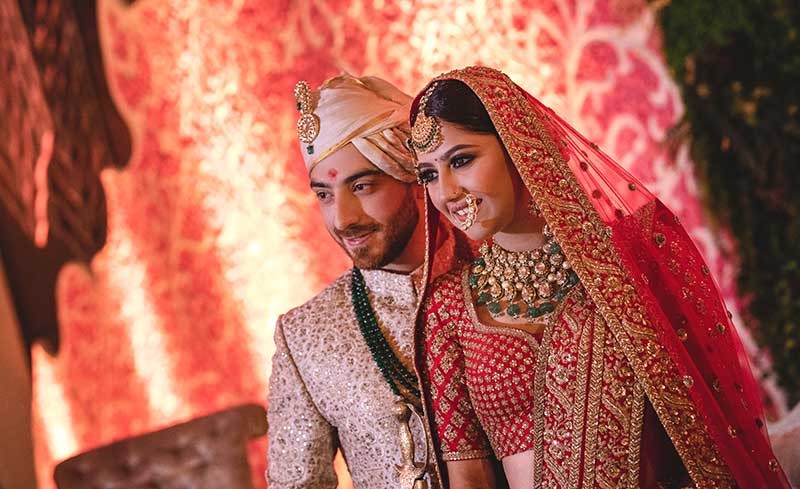 Priyansh and Priyanka embracing in warm red lighting at their wedding